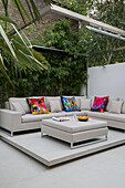 Bright cushions on corner sofa with bamboo in Victorian townhouse garden London UK