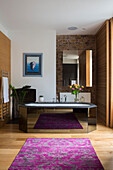 Large mirror on exposed brick wall with black bath and patterned rug in Victorian London townhouse UK