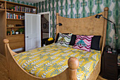 Tropical furnishings on wooden bed with bookcase in bedroom of Victorian London townhouse UK