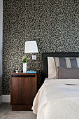 Geometrische Tapete mit Nachttisch aus Holz im Schlafzimmer eines Londoner Hauses UK