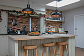 Black pendant lights above breakfast bar with wooden stools in 1930s Arts and Crafts home West Sussex UK