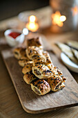 Sausage rolls on wooden board with lit candles in Arts and Crafts home West Sussex UK