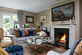 Glass coffee table and sofa in front of lit fire with artwork in Wiltshire living room