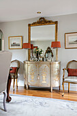Orange lamps and gilt framed mirror on decorative vintage cabinet in Wiltshire home England UK