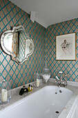 Gold and turquoise wallpaper with vintage mirror with marble bath surround in Wiltshire home England UK