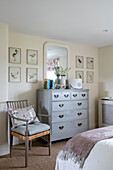 Artwork with mirror on painted chest of drawers with chair in bedroom of Somerset farmhouse UK