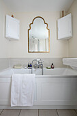 Vergoldeter Spiegel und Eckschränke über einer weiß getäfelten Badewanne in einem Bauernhaus in Somerset, UK