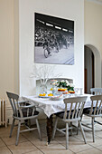 Large cycling print above kitchen table with grey painted chairs in detached Kent home UK