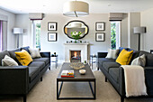 Zwei graue Sofas mit gelben Kissen und Couchtisch im Wohnzimmer eines Hauses in Surrey, Großbritannien