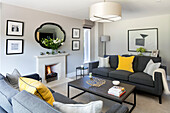 Pair of grey sofas with yellow cushions and lit fire in living room of Surrey home UK