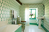 Green and white patterned wallpaper with chrome towel rail and bath in Somerset home UK