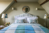 Hellblau karierte Decke auf Doppelbett mit rundem Spiegel in einem Haus in Somerset, UK