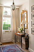 Wooden table and umbrella stand with gilt framed mirror at front door of Hampshire home UK