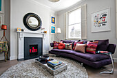 Curved purple sofa with low table and circular mirror in North London home UK