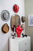 Collection of sunhats and mirror with red vase on chest of drawers in North London home UK