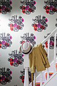 Hat and coat on banister with large floral motif wallpaper in North London home UK