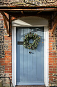 Selbstgemachter Kranz an der Tür, bemalt mit Wacholderesche Denkmalgeschütztes Cottage aus Ziegeln und Feuerstein aus dem Jahr 1500 in Hampshire, Großbritannien
