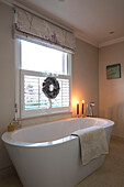 Lit candles on freestanding bath with Christmas wreath in East Dulwich Edwardian home London UK