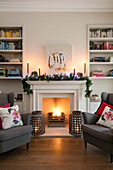 Graue Sessel mit Kissen von Philippa London und Bücherregale mit beleuchteten Laternen in einem Haus in East Dulwich, London, UK