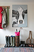 Mäntel und Stiefel mit Schirmständer und großer Leinwand einer Kuh in einem Haus in Hampshire UK