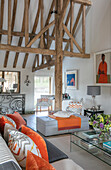 Orangefarbene Kissen auf einem Sofa mit Glastisch und Balkendecke in einem Haus in Hampshire, Großbritannien