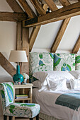 Green and blue upholstered headboard and chair with lamp at bedside in Hampshire home UK