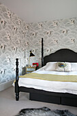 Black lamp and double bed with stork patterned wallpaper in London home UK