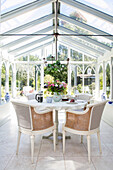 Korbstühle am Tisch mit Schnittblumen und Kaffeetasse im Wintergarten in Sussex UK