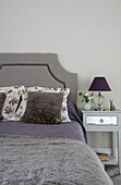 Grey headboard and blanket with purple lamp at bedside in Sussex home UK