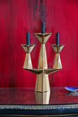 Gold candlestick with black candles set against red canvas in London home UK