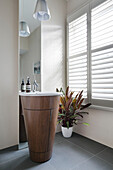 Freestanding wooden basin with mirrored wall and shutters in London home UK