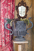 Urne mit Weintrauben, antikem Spiegel und roten Vorhängen in einem Haus in Sussex