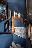 Gerahmte Bilder und goldener Stoff im blauen Treppenhaus eines Hauses in Sussex