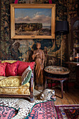Gilt framed art on tapestry wall with antique sofa and leopard skin rug in Sussex home