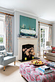 Dried hydrangeas in fireplace with canvas and buttoned ottoman in Hampshire home England UK