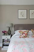 Floral cushions on double bed with bedside cabinet in Hampshire home England UK