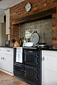 Dunkelgrauer Ofen und weiße Schränke mit freiliegender Ziegelwand in der Landhausküche von Kent UK