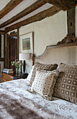 Wicker headboard and beige cushions with fur throw in timber framed Kent farmhouse UK