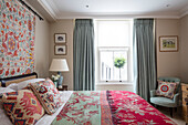 Doppelbett mit hellgrünen Vorhängen und Stuhl und handgefertigten Textilien in einer Wohnung im Norden Londons UK