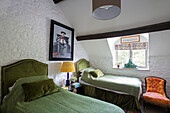 Twin beds with upholstered chair in bedroom of 1840s Cotswolds cottage Oxfordshire UK