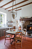 Marble topped table with terracotta floor tiles and lit fire below high beamed ceiling in French chateau Lot et Garonne
