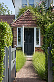 Open gate and brick path to porch of 1930s semi-detached cottage Surrey UK