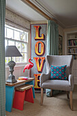 Einzelner Schriftzug 'LOVE' mit bemalten Beistellhockern und upgecyceltem Stuhl am Fenster eines denkmalgeschützten Bauernhauses in Bodmin, Cornwall, Großbritannien