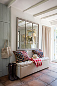 Blanket box with Moroccan cushions and large mirror in hallway of Surrey cottage UK