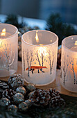 Three lit candles with frosted pine cones and baubles on windowsill in Berkshire cottage UK