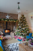 Weihnachtsgeschenke unter dem Baum mit beleuchtetem Holzofen in einem Haus in Surrey (UK)