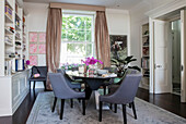 Grey dining chairs at oval table with bookshelf and gold curtains in London townhouse UK