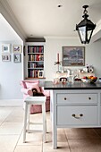 White and pale blue kitchen with dark grey worktop and pale pink armchair with dog in elegant Hampshire home UK