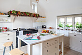 Weihnachtsgirlande über dem Ofen mit offenem Rezeptbuch auf einer Kücheninsel in einem Landhaus in Surrey, UK