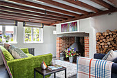 Grünes Sofa mit Kaminholz und offenem Ziegelsteinkamin Surrey UK